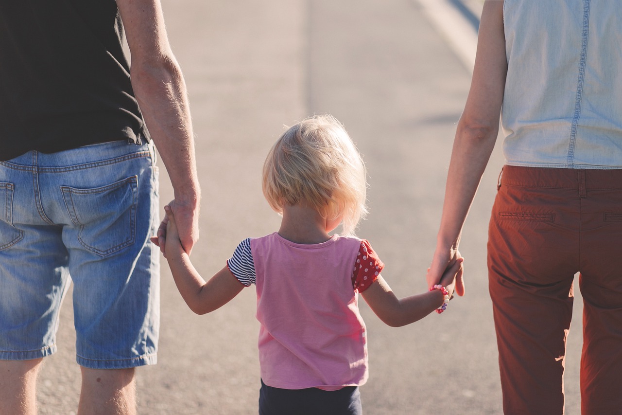 Una famiglia di spalle: due genitori che tengono per mano loro figlio mentre camminano
